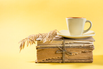 A cup of coffee on old books and dry ears of corn in yellow. Wellness, harmony, quiet reading. Copy space
