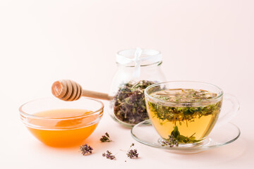 Fresh hot tea with oregano in a cup, honey in a bowl and dry herb in a jar. Herbal medicine and...