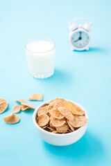 A bowl of cereal, a glass of milk and an alarm clock on a blue background. Scheduled breakfast....