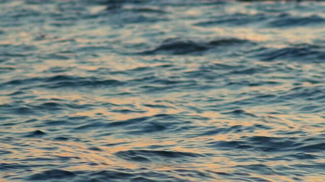 Sea, ocean surface with small waves and sunrise, sunset beams reflecting on the surface