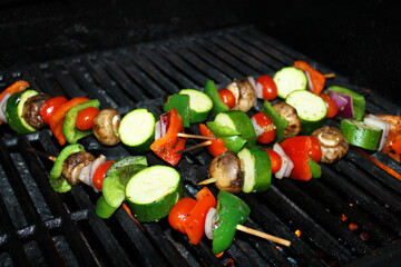 Close-up of vegetable skewers, with mushroom, onions, green pepper, red pepper, cherry tomatoes, Zucchini, and seasoning, on a barbecue grill.