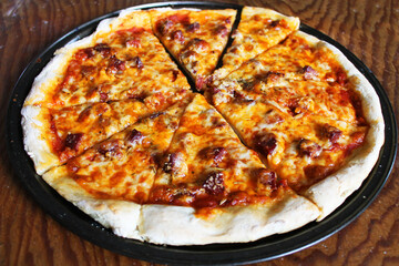 Close-up of fresh baked, homemade pizza, still on pan, on wooden cutting board.