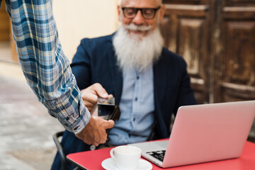 Senior hipster man paying with contactless credit card outdoors at var restaurant - Focus on waiter...