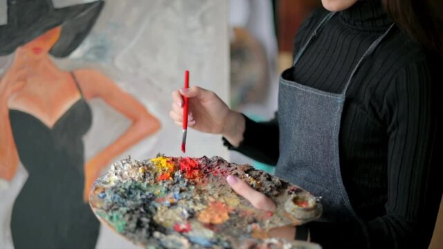 Woman painter wearing black clothes painting woman model face with hat drawing with red brush at a workshop