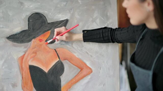 Woman painter wearing black clothes painting woman model face with hat drawing with red brush at a workshop