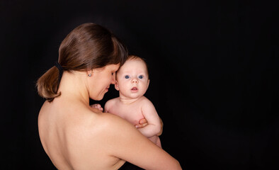 Sensual mom and baby hugging. Mother holding beautiful baby son. Happy mother kissing baby boy. Mother caring after her babys skin. Tenderness. Beautiful image of maternity. Studio shot. Babycare