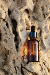Amber glass spray bottle with white blank label on rock stone on beige background. Natural organic cosmetic product mockup. Flat lay, top view. sunset light