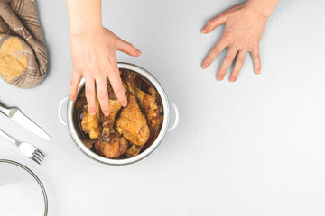 Hungry child pulls his hand for food, concept, roasted chicken in a saucepan, kitchen workspace background, top view and copy space