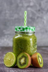 Healthy fresh fruit smoothie drink surrounded by kiwi lime and lemon on gray