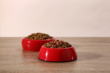 Dry food in red pet bowls on wooden surface