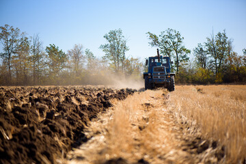 Agriculture blue tractor plowing in autumn on the field.