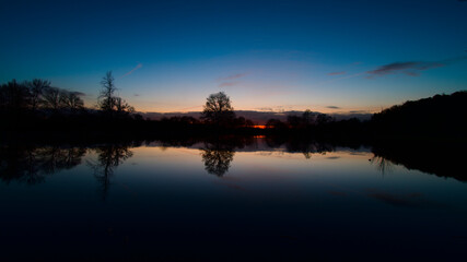 Fototapeta premium Lever de soleil et son reflet sur de l'eau des marais de Bazouges cré sur Loir avec silhouette d'arbres en fond