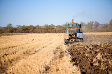 Fototapeta premium Tractor seeding directly into the stubble after the harvest with blue sky during autumn day.