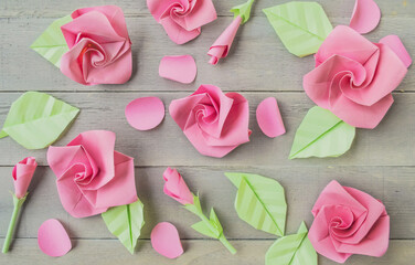 Origami paper background with flowers and leaves. Handmade pink roses backdrop. Origami composition. Paper craft.