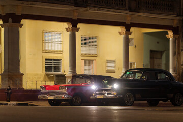 Fototapeta na wymiar Amazing old american car on streets of Havana with colourful buildings in background during the night. Havana, Cuba.