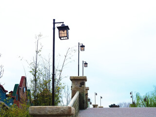 Decorative street lamps line up along the bridge in the park against the backdrop of a cloudy sky.