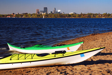 Kayaks rest along the shore of a lake within sight of the Minneapolis skyline