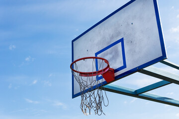 Basketball hoop with torn net against blue sky.