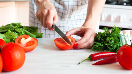 A young woman cuts a ripe tomato with a knife for salad. Healthy food concept. Close-up.