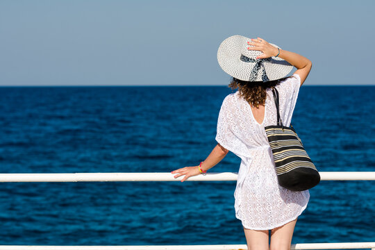 Woman enjoying travel vacation at sea. Gril with white hat and bag looking at sea.