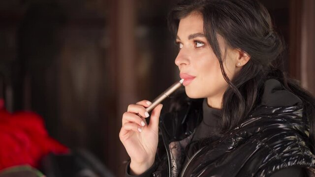 Woman Smoking tobacco heater system dressed black jacket close up portrait