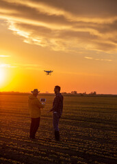 Fototapeta premium Two satisfied farmers standing in field using drone