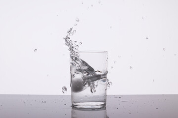A piece of ice makes a splash in a glass of water.