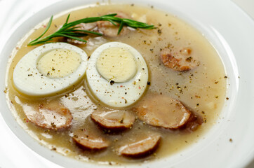 Traditional polish sour soup with sausage and eggs in a white deep plate