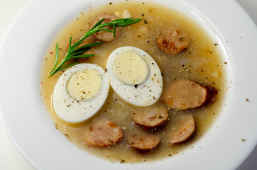 Traditional polish sour soup with sausage and eggs in a white deep plate