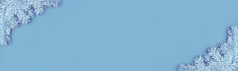Christmas banner with pastel colored festive corner borders of fluffy light blue fir branches on blue background. Trendy monochrome xmas template. Top view, flat lay style, copy space for text.