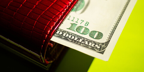 Hundred dollar bill sticking out of a red purse closeup