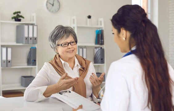 Cheerful senior lady discussing course of treatment with her doctor. General practitioner and mature woman talking and looking at each other during interview in medical office of clinic or hospital