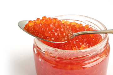 Red caviar in glass jar with spoon on top. Texture of salmon caviar. White background, close up. 