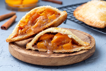 Small peach and cinnamon hand pies with crust dough, sprinkled with sugar, on wooden plate closeup, horizontal