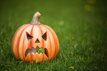 Pumpkin shaped ceramic candlestick on green grass. Funny Carved Pumpkin in the garden, halloween background