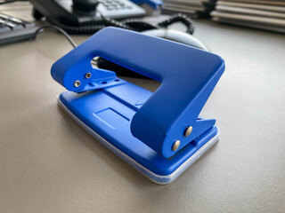 Blue iron metal office punch for punching holes in sheets of paper and documents on the working business table in the office. Stationery