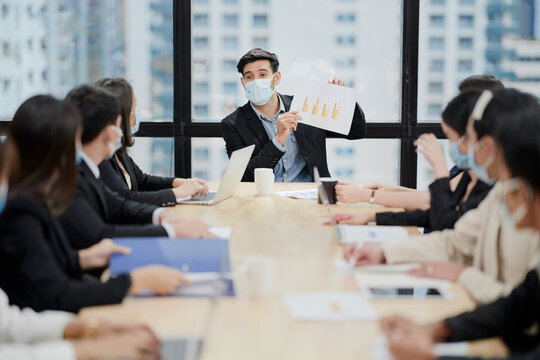 In a meeting room, a sales manager is discussing sales forecast with his team during covid-19.