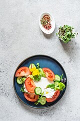 Appetizing salad with feta cheese, fresh vegetables (tomatoes, cucumbers, onions), crispy lettuce, microgreens and violet flowers. Non-standard serving of Greek salad.