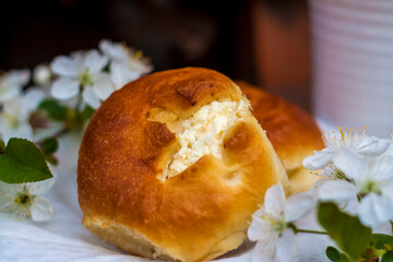 Baked open rolls and a cup of coffee on a dark, worn rustic wooden table. The composition is decorated with a twig with white flowers. Cherry tree flowers. Selective focus.