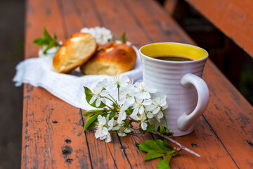Baked open rolls and a cup of coffee on a dark, worn rustic wooden table. The composition is decorated with a twig with white flowers. Cherry tree flowers. Selective focus.