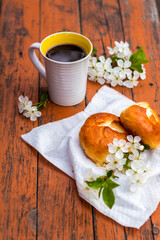 Baked open rolls and a cup of coffee on a dark, worn rustic wooden table. The composition is decorated with a twig with white flowers. Cherry tree flowers. Selective focus.