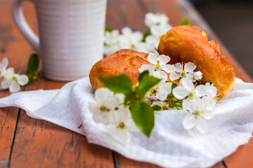 Baked open rolls and a cup of coffee on a dark, worn rustic wooden table. The composition is decorated with a twig with white flowers. Cherry tree flowers. Selective focus.