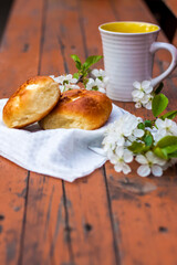 Baked open rolls and a cup of coffee on a dark, worn rustic wooden table. The composition is decorated with a twig with white flowers. Cherry tree flowers. Selective focus.
