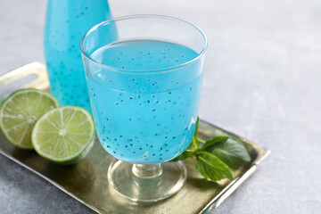 Tasty light blue drink with basil seeds on grey table