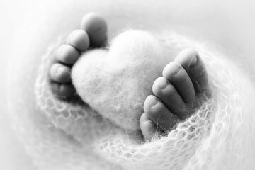 Feet of a newborn with a wooden heart, wrapped in a soft blanket. Black and white studio photography.