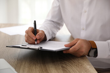 Businessman signing document at table indoors, closeup