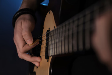 Man playing electric guitar on dark background, closeup. Rock music