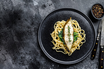 Obraz na płótnie Canvas Spaghetti pasta with Halibut fish steak and spinach. Black background. Top view. Copy space