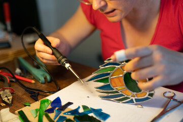 young woman soldering a stained glass window, peacock feathers, female craftsman, making stained...