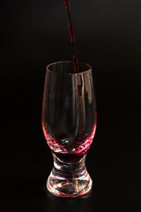 Red wine is poured into a transparent glass on a black background. The glass is filled with red wine